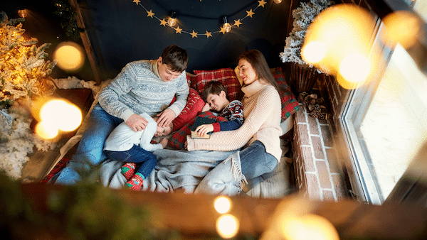Family cuddled on floor with Christmas lights around them
