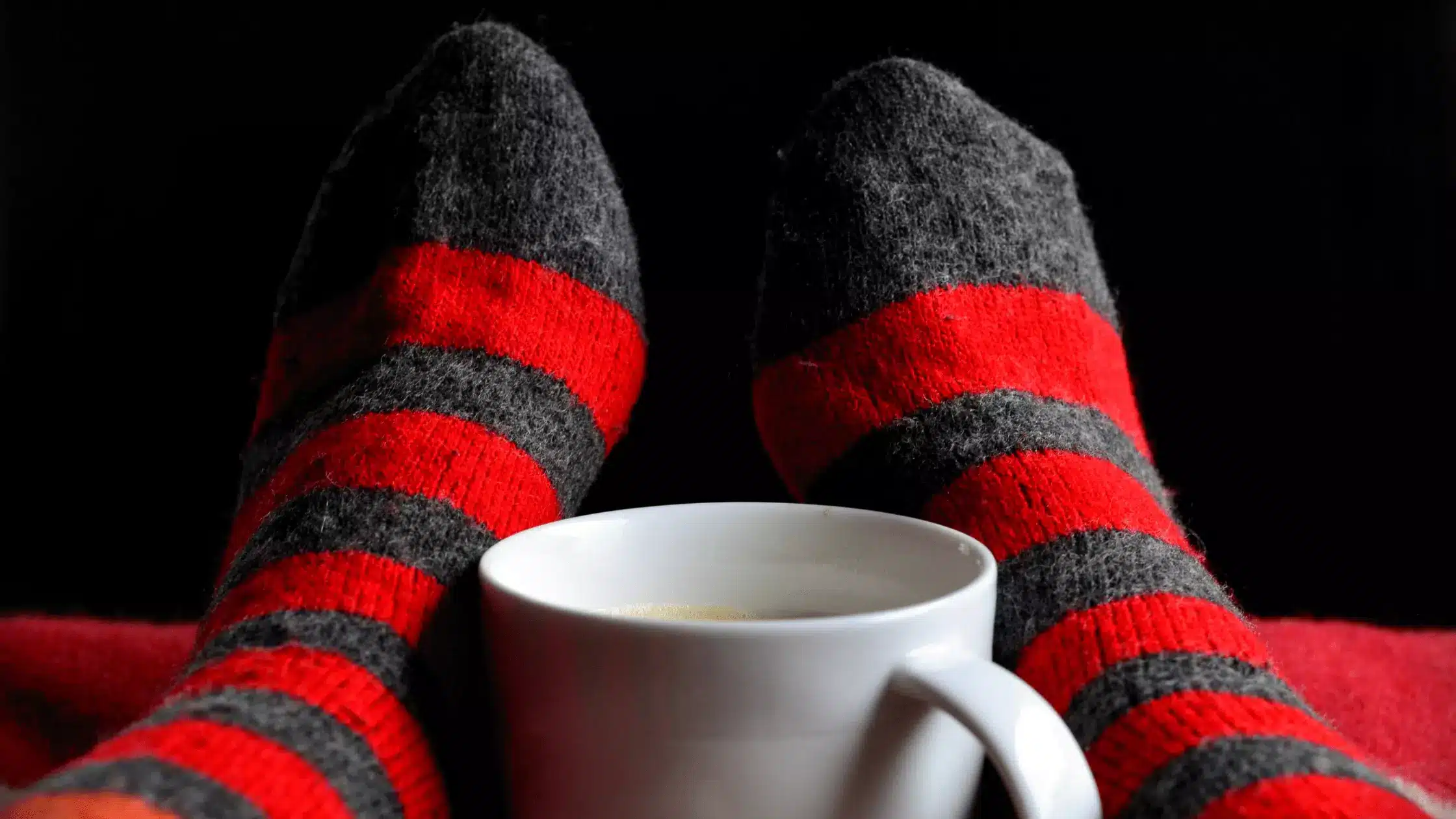 Warm socks on feet with a coffee mug between them