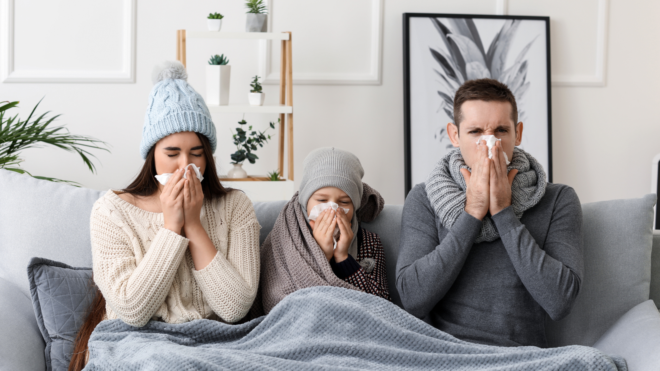 Family sick with flu - hands with tissues to their noses while they sit on the couch